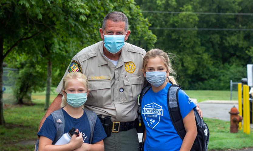 A school resource officer smiles while standing with two students